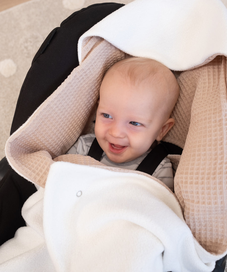 Temperaturregulierender Wendestoff*Für jede Temperatur geeignet: Der weiche Teddystoff wärmt dein Baby, der Waffelpiquet hat eine kühlende Wirkung an warmen Tagen.|Baby in Babyschale mit Einschlagdecke zum Wenden.