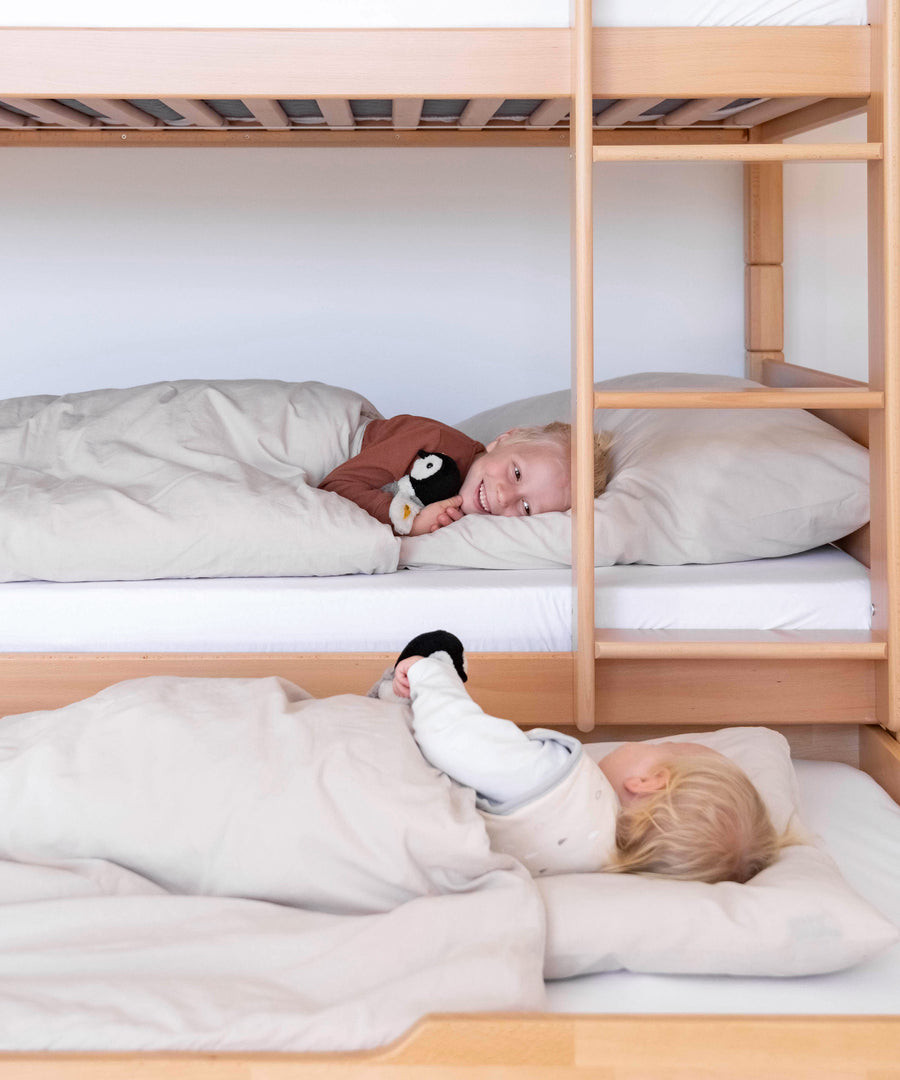 Zusätzlicher Schlafplatz*Für Übernachtungsgäste oder Eltern: Mit dem optionalen Bettkasten kann man ganz einfach einen weiteren Schlafplatz zaubern.|Mädchen sitzt im unteren Bett des Etagenbetts, auf dem ausgezogenen Bettkasten davor sitzt ein Geschwisterkind.