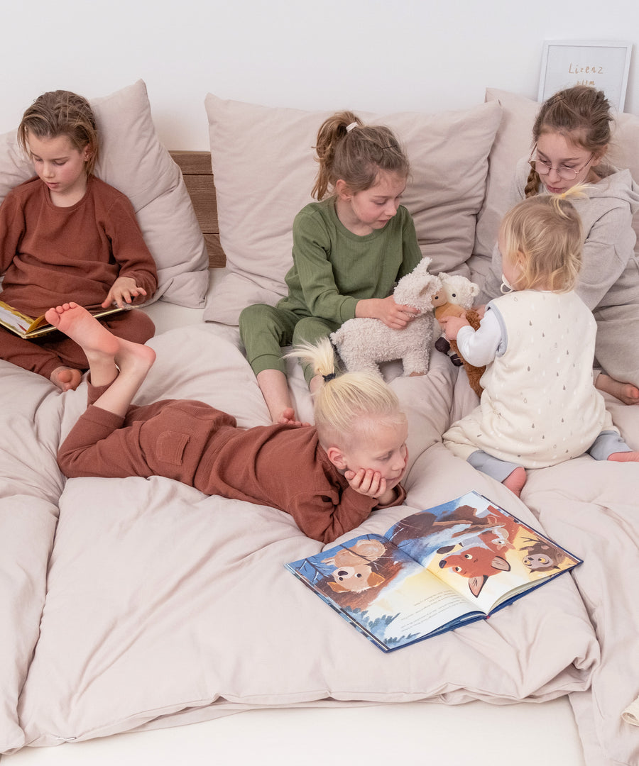 Das perfekte Familienbett*Flexibel dank modularer Bauweise und passend für jedes Zuhause: Unser Bett ist in zwei Höhen und drei Ausführungen erhältlich.|Kinder sitzen auf Familienbett Esche bodentief.