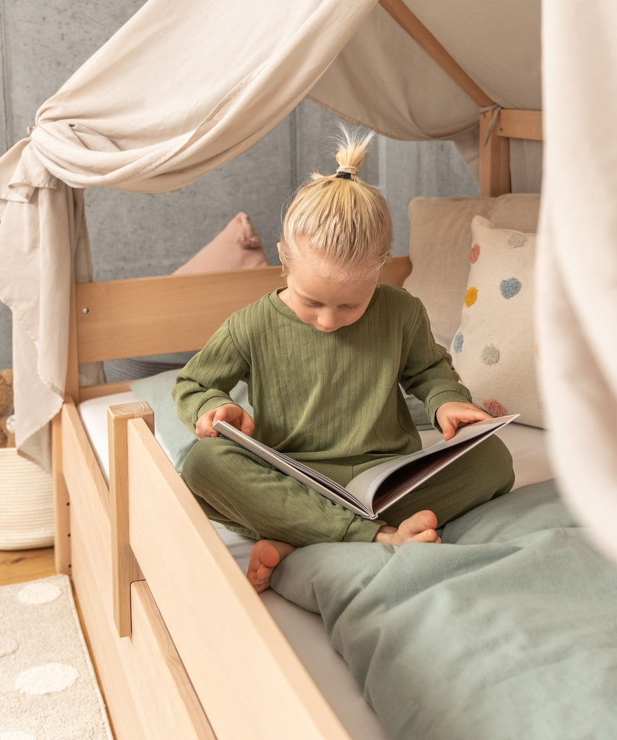 Kind sitzt im Hausbett und liest ein Buch.