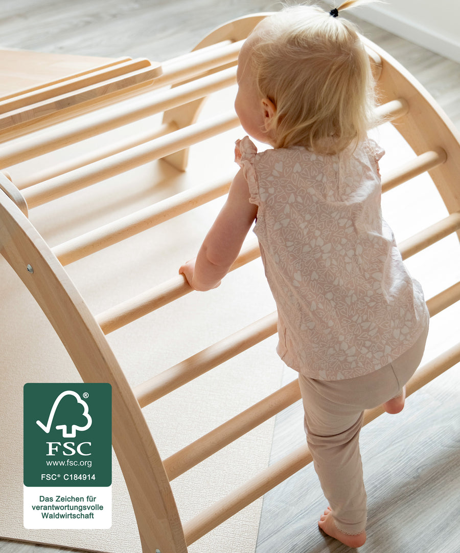 Fördert die Entwicklung*Der Kletterbogen fördert erste Stehversuche sowie die Motorik beim Klettern und schult dabei die Bewegungssicherheit.|Kleinkind klettert auf Kletterbogen, Kletterbogen ist spiel gut zertifiziert.