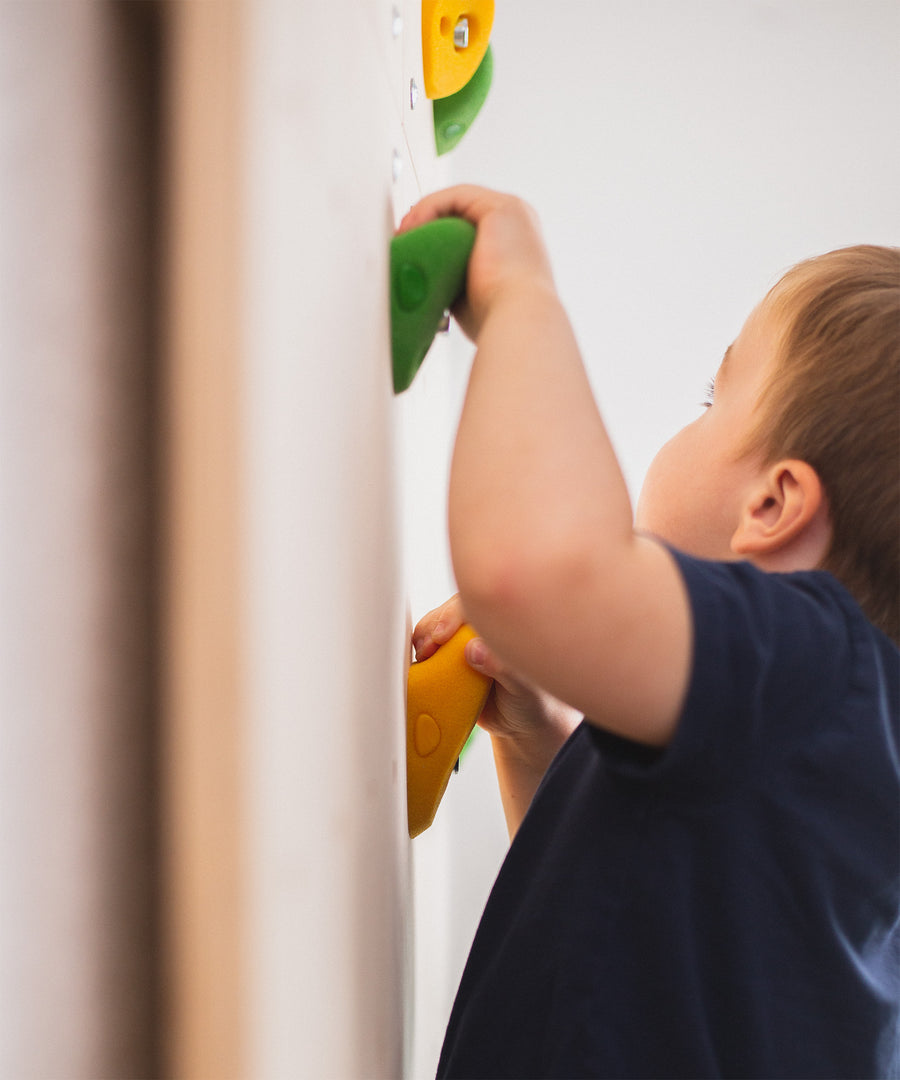 Kind klettert an Kletterwand für Kinder und greift nach Klettergriffen.