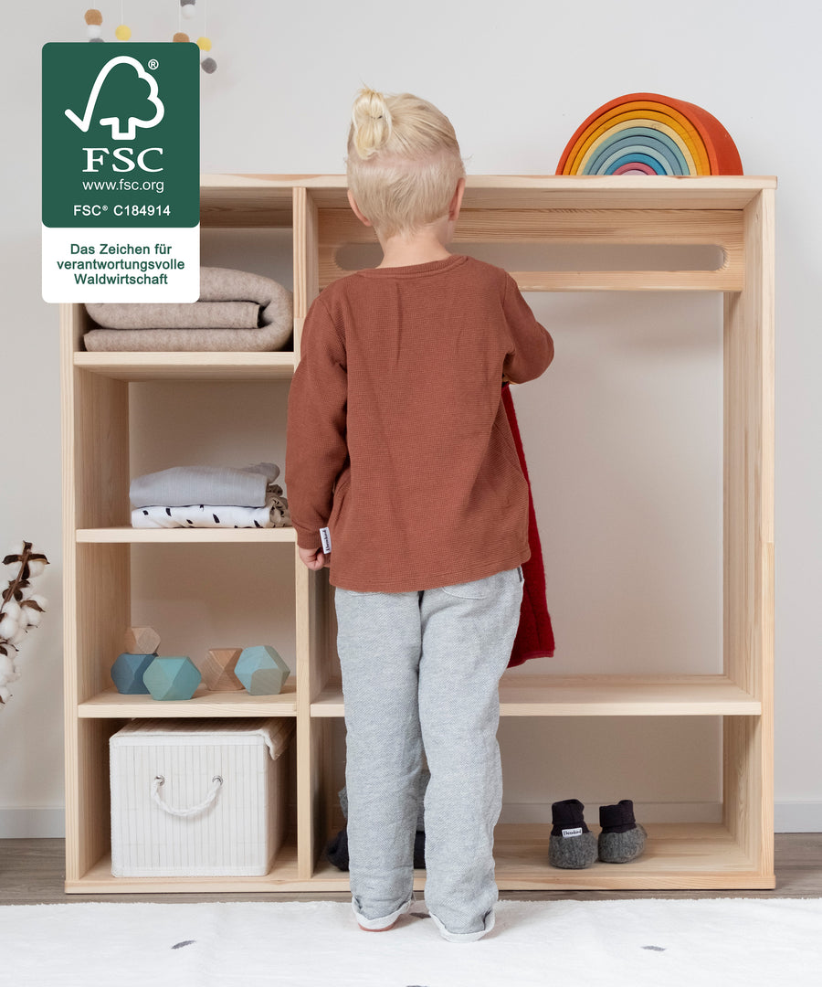 Kind hängt Kleidungsstück alleine in Montessori Kleiderschrank.