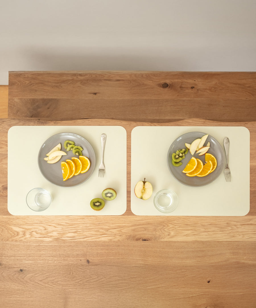 Perfekte Unterlage beim Essen*Das Tischset ist der optimale Schutz für deinen Esstisch - erhältlich in zwei Größen als praktisches 2er-Set und 4er-Set. Tischset in Salbeiweiß.|Zwei Tischsets schützen die Holzoberfläche, jedes mit einem Teller voller Obst und einem Glas Wasser.