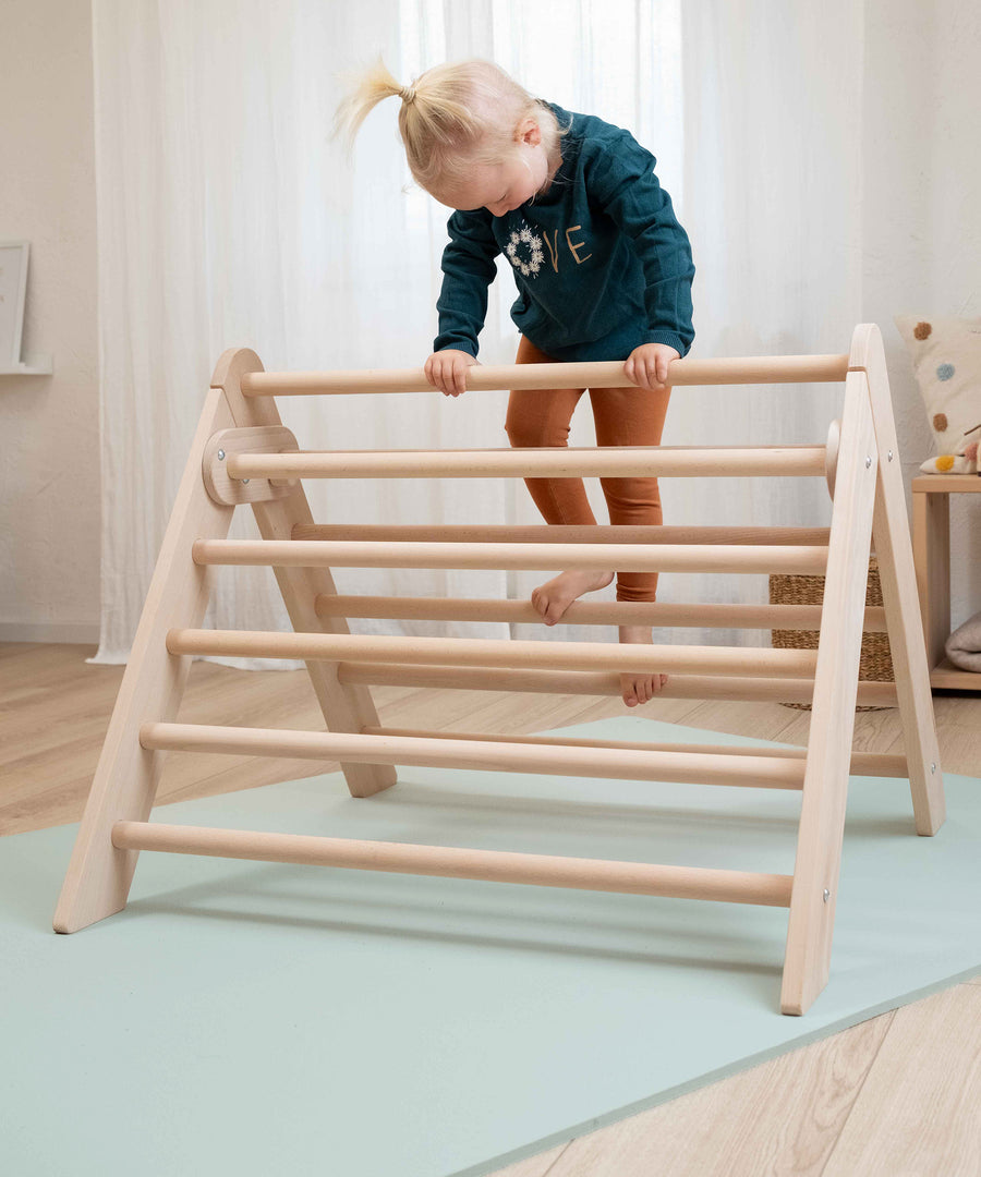 Kind klettert auf ein Kletterdreieck, das auf einer Krabbelmatte steht.
