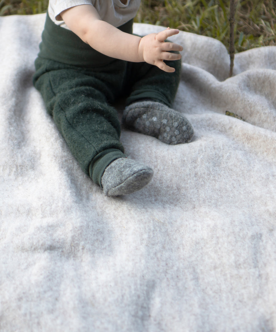 In Bio-Qualität*Die Decke aus traditionell gewalkter Bio-Schurwolle und -Baumwolle ist angenehm leicht und 100% mulesingfrei.|Baby sitzt auf einer Walkdecke.