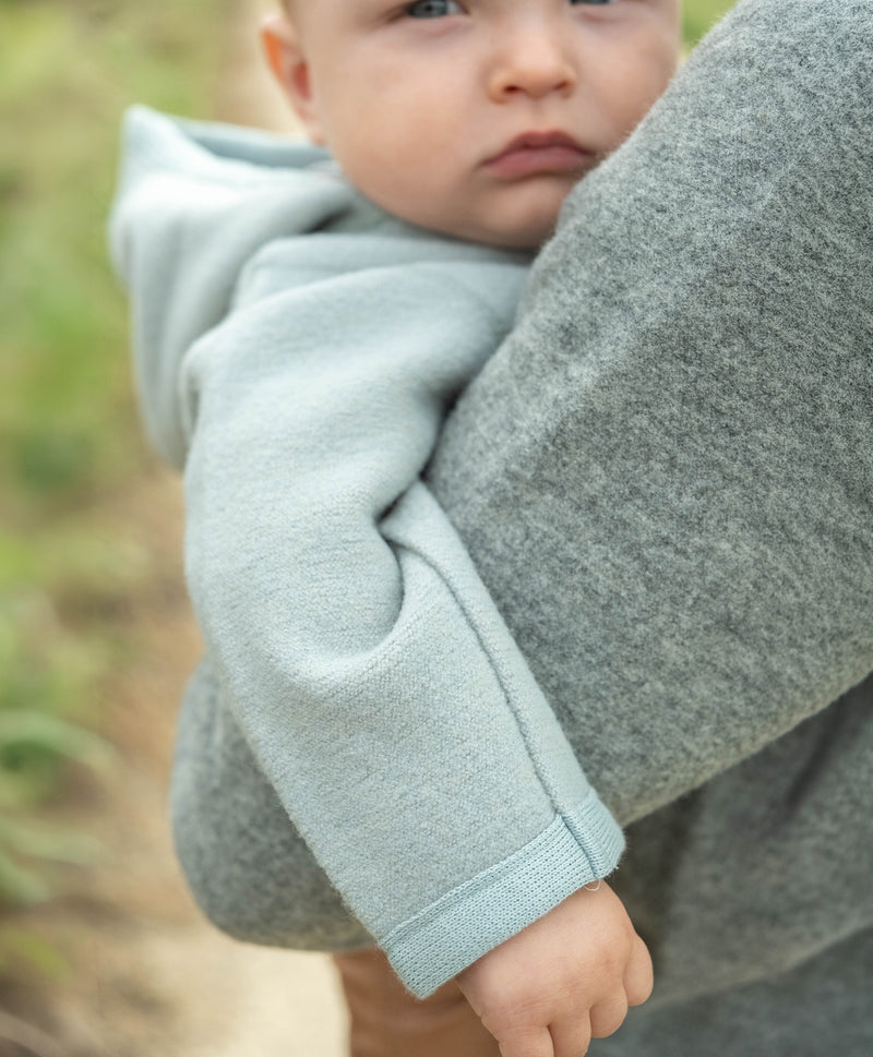 Kind in Walkjacke Jade auf Arm von Mutter in Walkjacke Grau