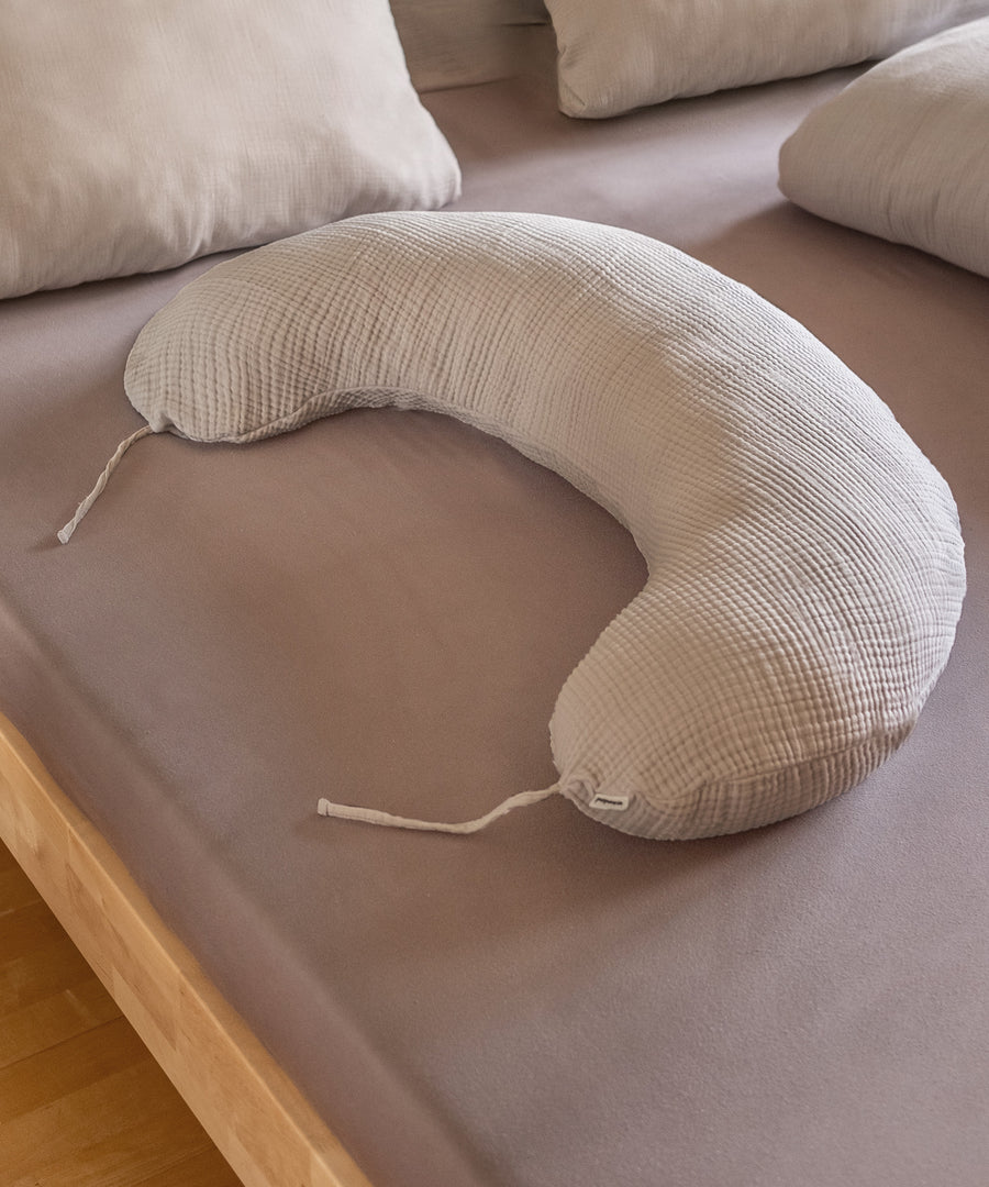 Allround-Talent Stilkissen*Schon während der Schwangerschaft kann das Stillkissen als Seitenschläferkissen oder Lagerungskissen unterstützend wirken.|Stillkissen mit Faserbällchen liegt auf Bett.