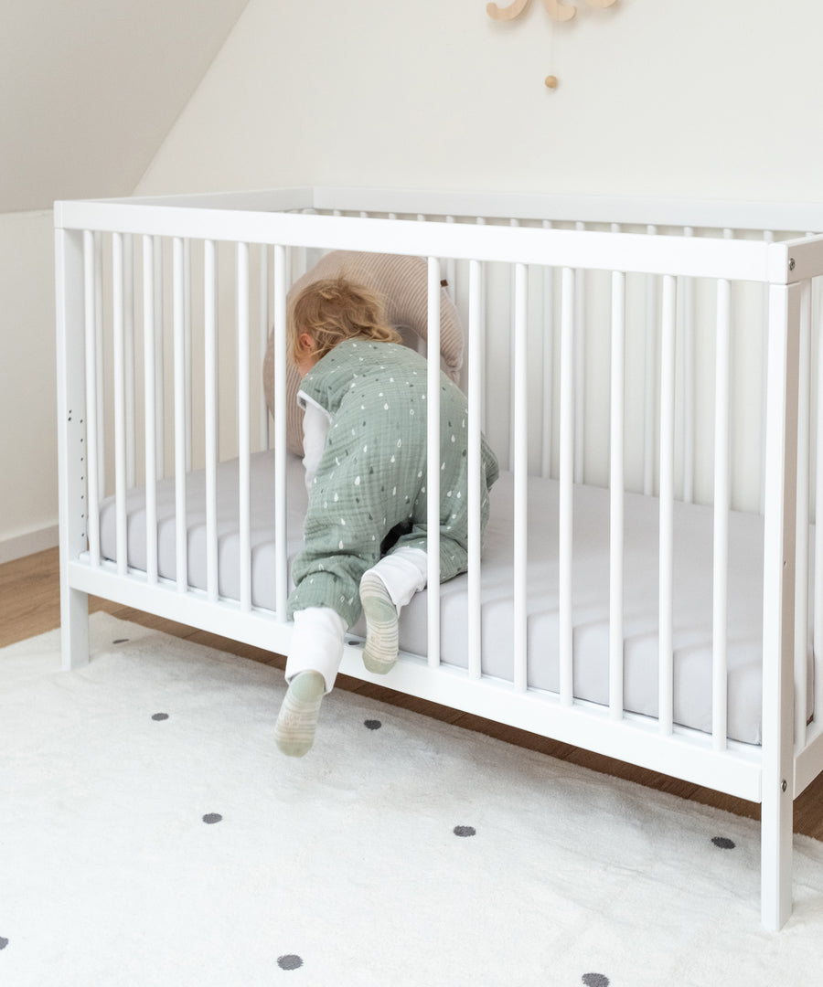 Fördert die Selbstständigkeit*Durch die herausnehmbaren Stangen kann dein Kind ganz alleine ein- und aussteigen. Der Rausfallschutz bleibt dabei erhalten.|Kind krabbelt durch Öffnung in Babybett weiß.
