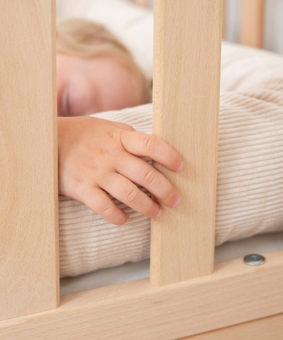 Kind schläft im Kinderbett mit Bettschlange in Beige.