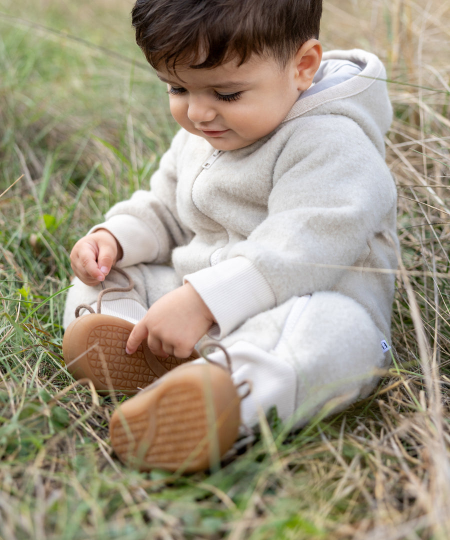 Leicht und flexibel*Das weiche Außenmaterial sowie die flexible Sohle sind äußerst leicht und unterstützen dein Kind beim Laufenlernen.| Kind sitzt im Feld und trägt die Lauflernschuhe Wollfilz.