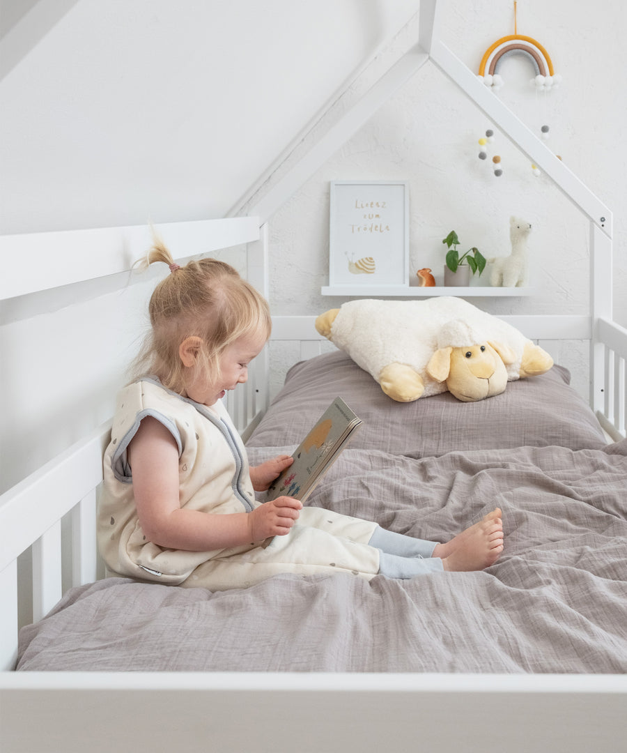 Mädchen sitzt in Hausbett Kiefer Weiß und schaut ein Buch an.