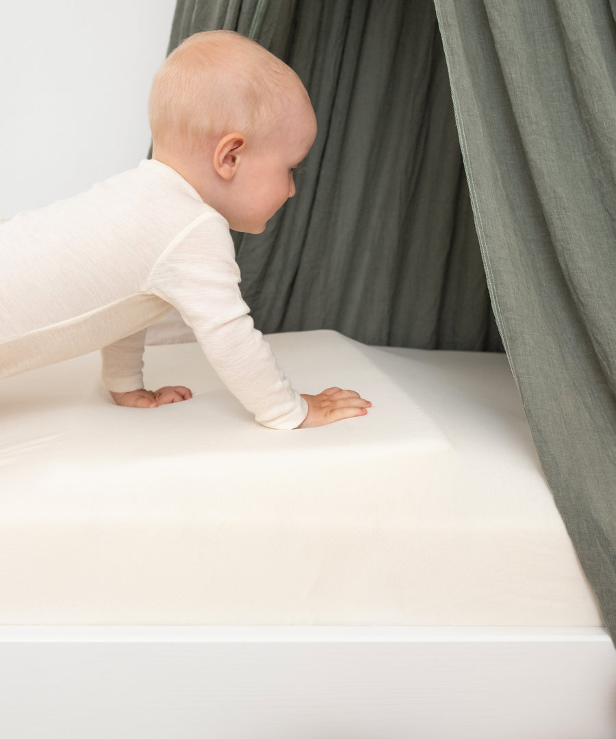 Made in Europe*Gefertigt in der EU besteht das Keilkissen aus OEKO-TEX® STANDARD 100 zertifizierten Materialien - speziell für Babys & Kinder.|Baby krabbelt auf Keilkissen im Bett.
