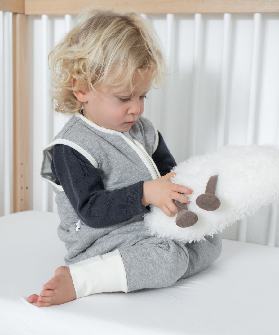 Kind sitzt im Bett und trägt den grauem Schlafsack.
