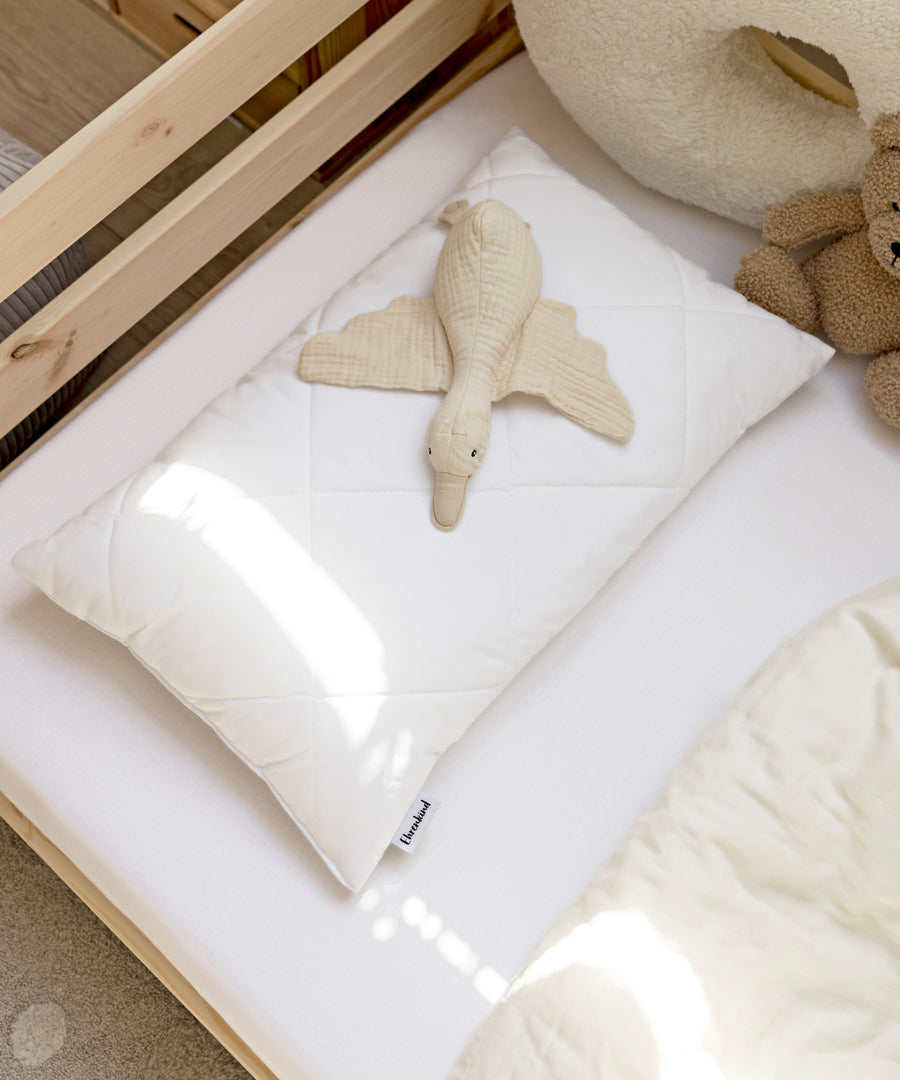 Kinderkissen mit Kuscheltier auf einem Kinderbett.