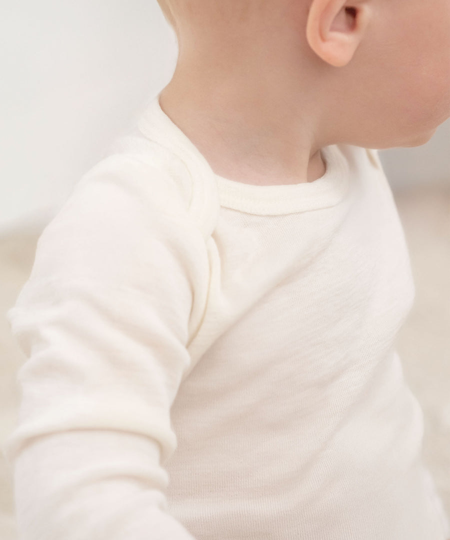 Fein, elastisch & weich*Die besonders feine und dünne Merinowolle ist sehr weich auf der Haut und trägt zu einem hohen Tragekomfort bei.|Sitzendes Baby mit Merinowolle-Body.