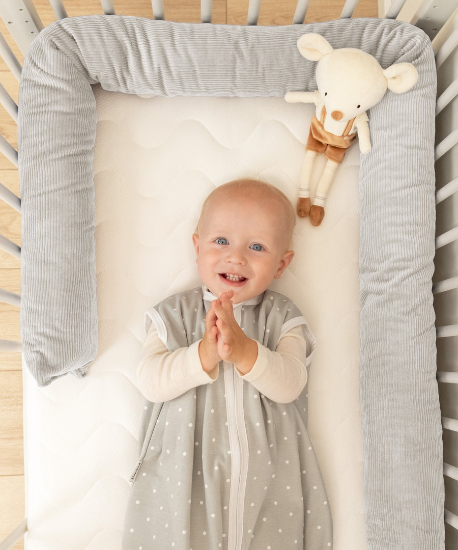 Geborgenheit von Anfang an*Die weiche Bettschlange schützt dein Baby vor Zugluft, Gitterstäben & sorgt für ein sicheres Schlafgefühl.|Baby liegt im Babybett umrandet von einer Bettschlange in Grau.