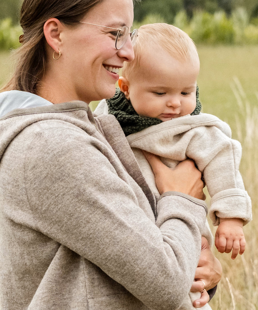 Praktisch & langlebig*Der Strickschal aus Naturwolle ist formstabil, robust und lässt sich kinderleicht über den Kopf ziehen.| Frau und Baby zusammen auf einem Feld und das Baby trägt den Schlauchschal Grobstrick in Oliv.