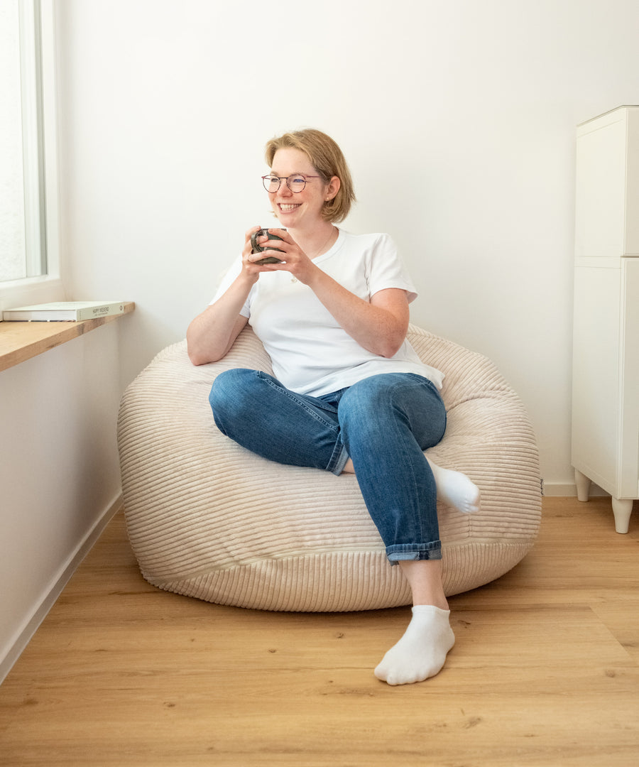 Entspannen leicht gemacht*Ideal zum Lesen, Spielen oder Relaxen - das flexible EPS-Granulat passt sich jeder Sitzposition ergonomisch an.|Frau sitzt im Sitzsack XXL in Natur und trinkt einen Kaffee.