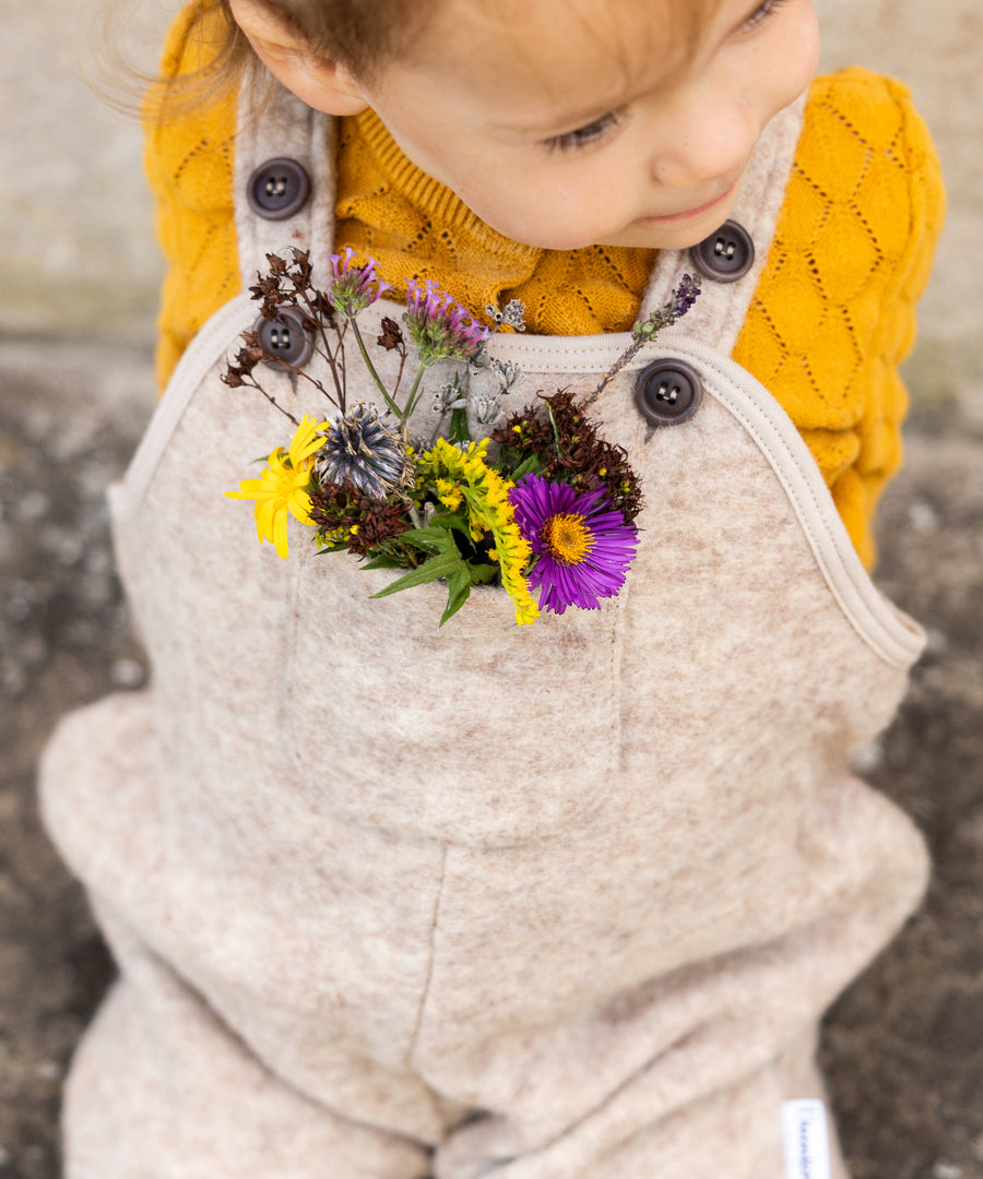 Warm eingepackt in die Natur*Der praktische Latzträgerschnitt hält Bauch und Rücken wohlig warm. Mit Brusttasche für kleine Schätze aus Wald & Wiese.| Kind trägt die Walk-Latzhose in Natur.