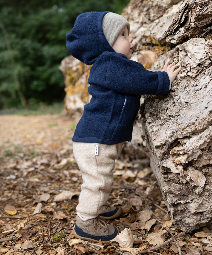 Kind trägt Walkjacke, Walkhose und Lauflernschuhe.