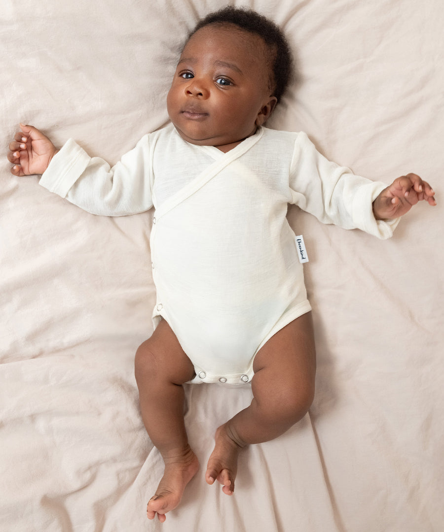 Klimaregulierende Eigenschaften*Merinowolle reguliert Feuchtigkeit, hält die Haut warm und trocken und kann so Hautausschlag bei Babys vorbeugen.|Baby liegt auf Bett.